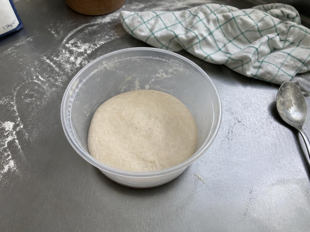 Flat, dense pizza dough sitting unrisen in a clear container