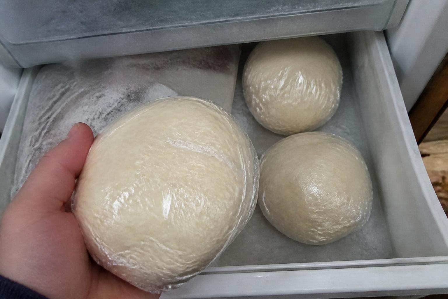 Wrapped pizza dough balls stored in a home freezer drawer