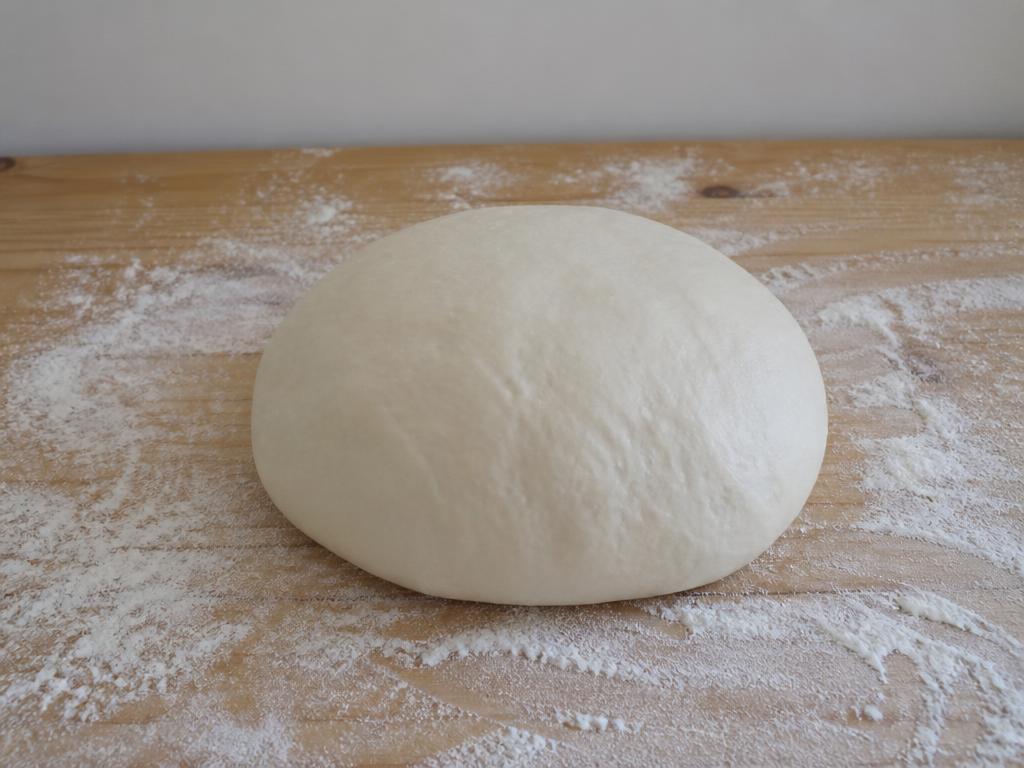 Properly proofed pizza dough ball holding a tight round dome on a floured wooden board