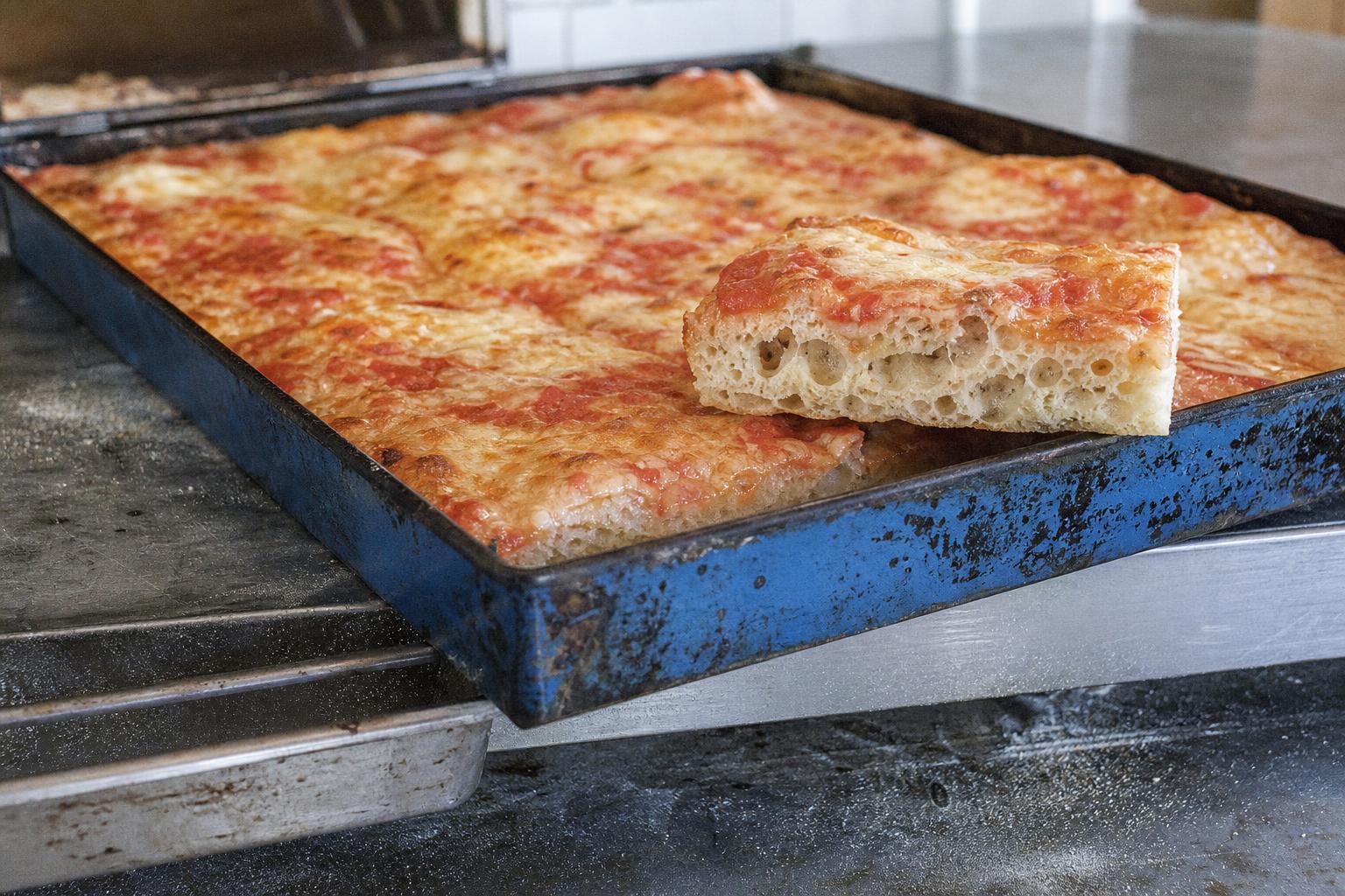 Pizza in Teglia in der typischen blauen Stahlform, ein herausgehobenes Stück zeigt die hohe, offene Krume